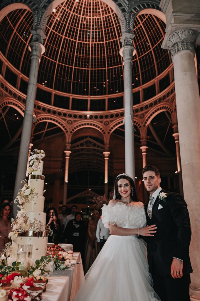 L and O wedding couple beside their cake in a glass conservatory, planned by Inspired By You