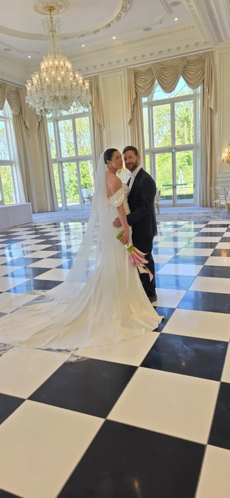 Bride and groom on a black and white chequered dance floor in a chandeliered ballroom, wedding planned by Inspired By You