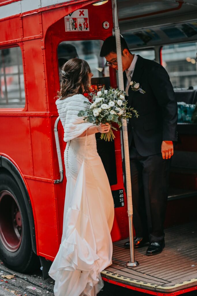 Bride and groom boarding a vintage red London bus on their wedding day