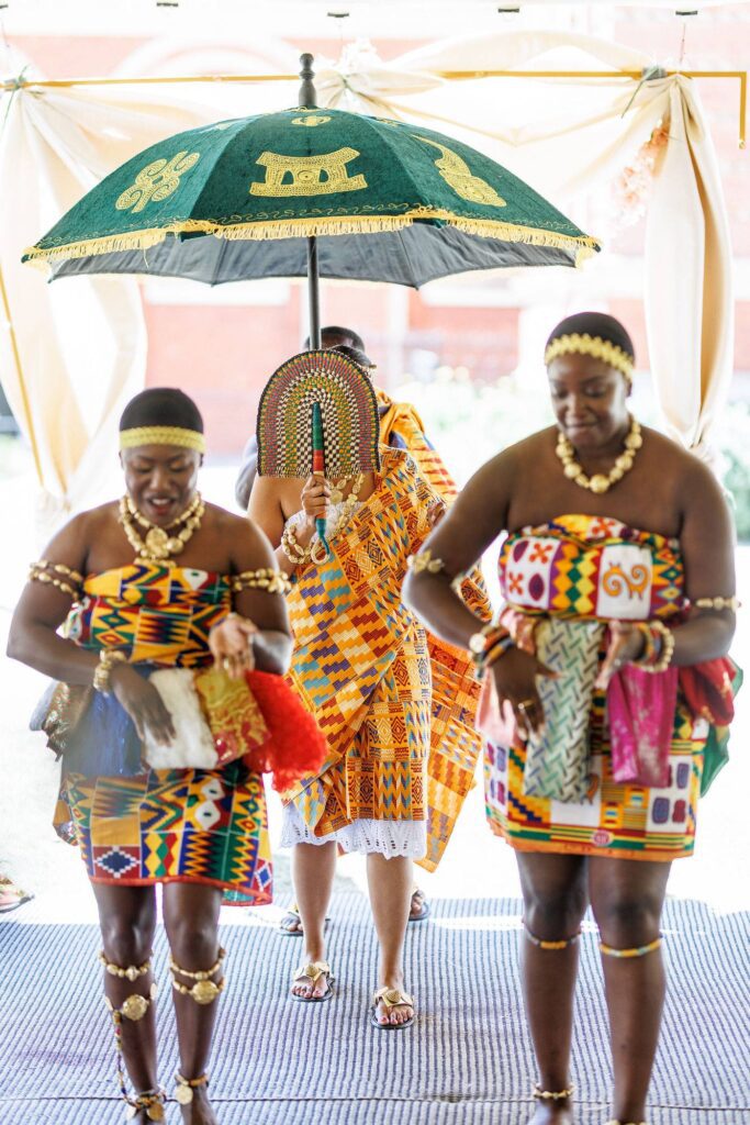 Bride arriving under a ceremonial umbrella at a traditional Ghanaian wedding ceremony