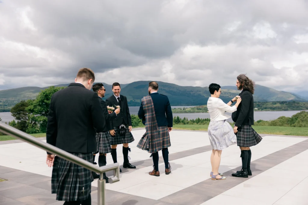 Wedding planner Oana pinning a groomsman’s buttonhole on a Scottish loch-side terrace